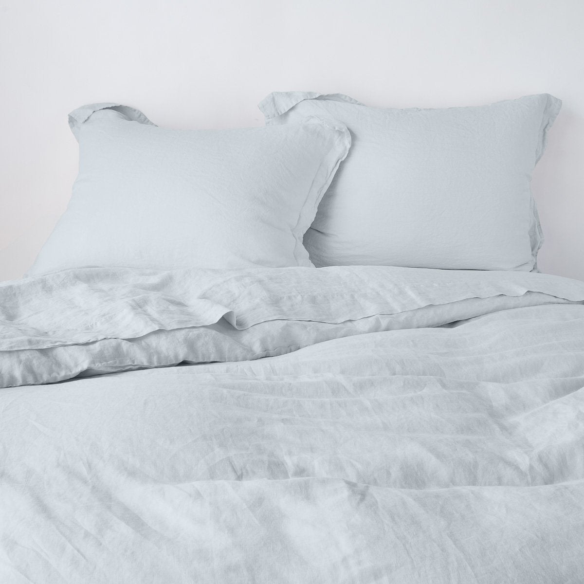 Linen Duvet Cover | Cloud | duvet cover partially folded back on a bed with matching sheets and shams against a white wall - cropped end of bed view.