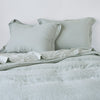 Linen Twin Duvet Cover | Eucalyptus | Linen duvet cover in eucalyptus, partially folded back on a bed with matching sheets and shams on a plain background - cropped end of bed view.
