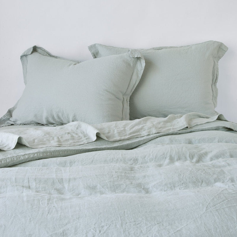 Linen Twin Duvet Cover | Eucalyptus | Linen duvet cover in eucalyptus, partially folded back on a bed with matching sheets and shams on a plain background - cropped end of bed view.