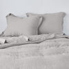 Linen Twin Duvet Cover | Fog | duvet cover partially folded back on a bed with matching sheets and shams against a white wall - cropped end of bed view.