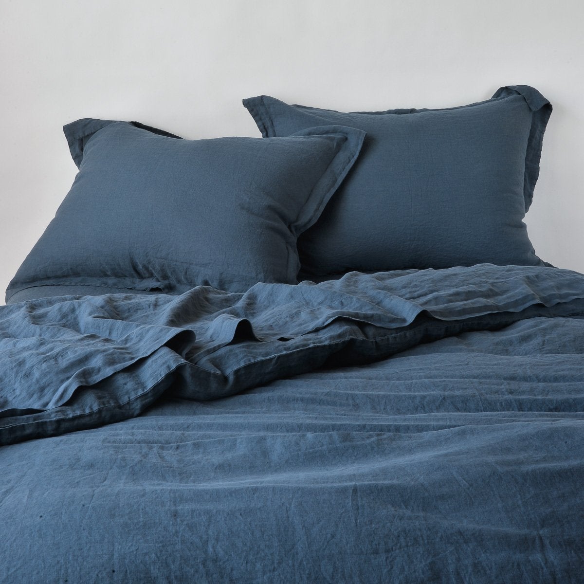 Linen Duvet Cover | Midnight | duvet cover partially folded back on a bed with matching sheets and shams against a white wall - cropped end of bed view.