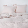 Linen Twin Duvet Cover | Pearl | duvet cover partially folded back on a bed with matching sheets and shams against a white wall - cropped end of bed view.