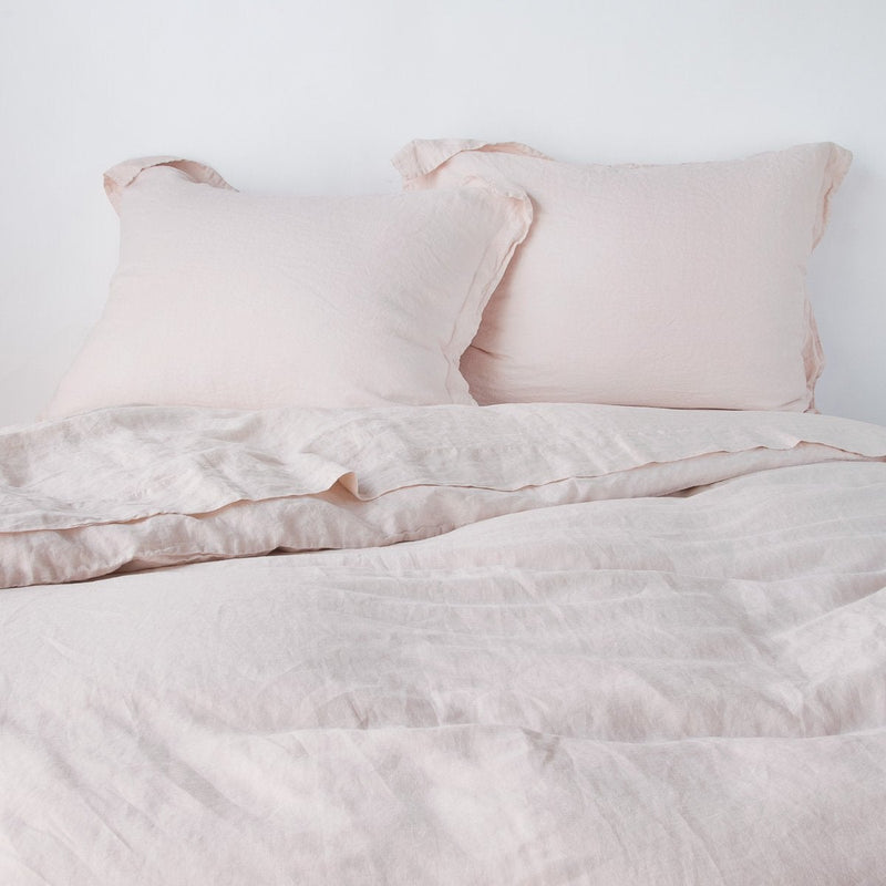 Linen Twin Duvet Cover | Pearl | duvet cover partially folded back on a bed with matching sheets and shams against a white wall - cropped end of bed view.