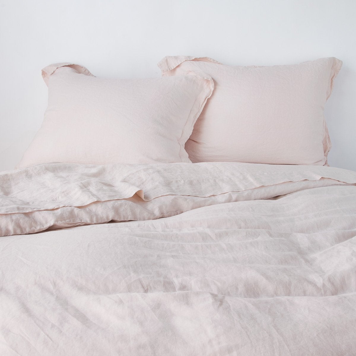 Linen Duvet Cover | Pearl | duvet cover partially folded back on a bed with matching sheets and shams against a white wall - cropped end of bed view.