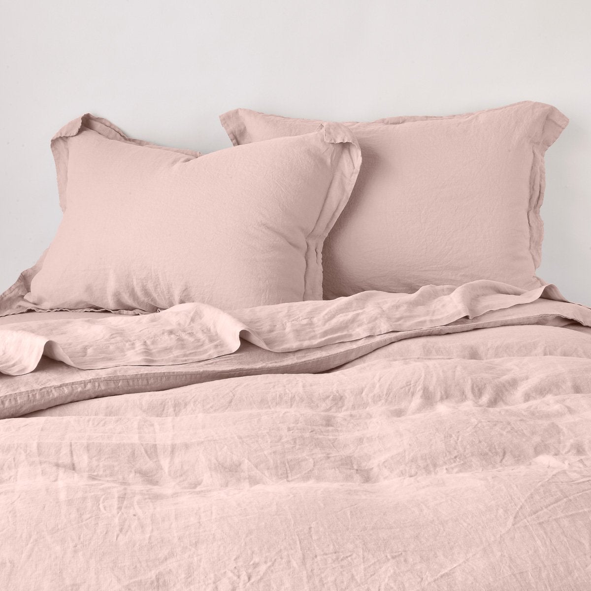 Linen Duvet Cover | Rouge | duvet cover partially folded back on a bed with matching sheets and shams against a white wall - cropped end of bed view.