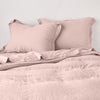 Linen Twin Duvet Cover | Rouge | duvet cover partially folded back on a bed with matching sheets and shams against a white wall - cropped end of bed view.