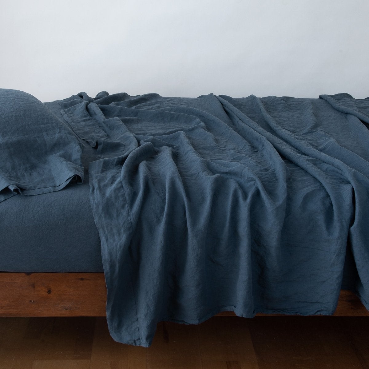 Linen Fitted Sheet | Midnight | fitted sheet with matching rumpled flat sheet and sleeping pillow - side view.
