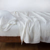 Linen fitted sheet in winter white, with matching rumpled flat sheet and sleeping pillow - side view.