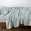 Linen Twin Flat Sheet | Eucalyptus | Rumpled linen flat sheet in eucalyptus, with matching fitted sheet and sleeping pillow - side view.