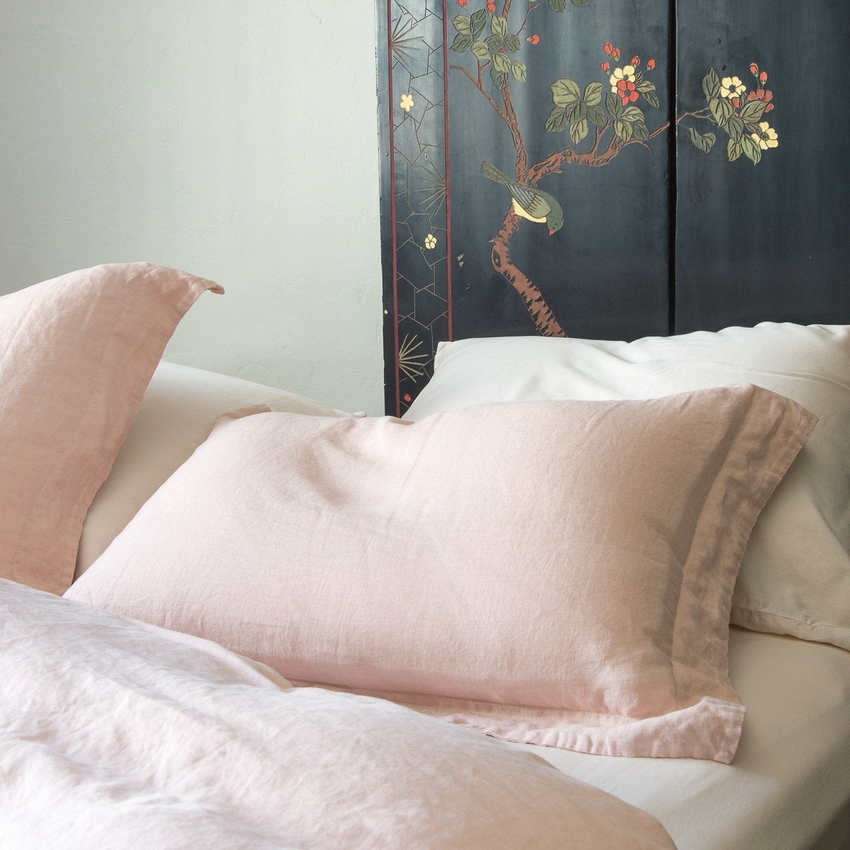 Close-up linen sham in pearl over white sheeting, highlighting simple yet elegant self flange - cropped three-quarter angle.