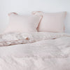 Linen Sham | Pearl | Two shams leaning upright against a white wall with matching sheeting and duvet - cropped end of bed view.