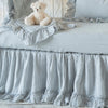 Linen whisper crib skirt in cloud, shown on a white iron crib with matching baby blanket and pillow - side view.