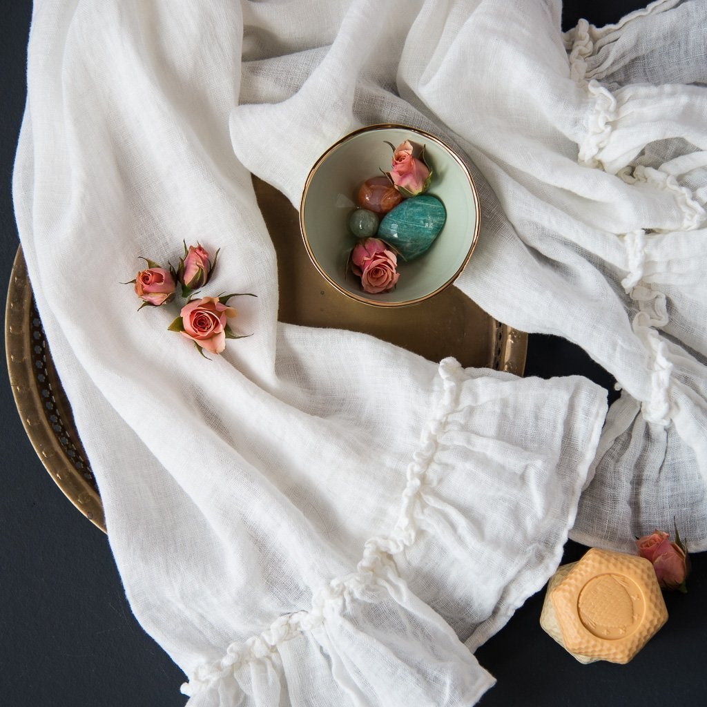 Winter White | Linen Whisper guest towel in winter white, draped over a dark background and tray with soft coral and green accessories - overhead view.