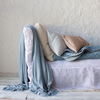 Loulah Blanket | Loulah throw blanket in cloud, draped over the side of a white linen day bed sofa, layered with light neutral pillows in a variety of textures.