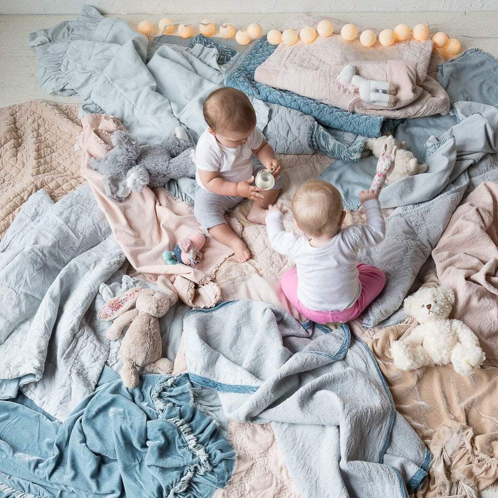 Loulah Baby Blanket | Two babies sitting and playing on a floor covered with rumpled blankets in a variety of textures of cloud, sterling, and pearl tones - overhead view.