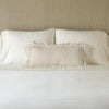 Loulah Throw Pillow | Parchment | pillow on a white bed - cropped end of bed view.