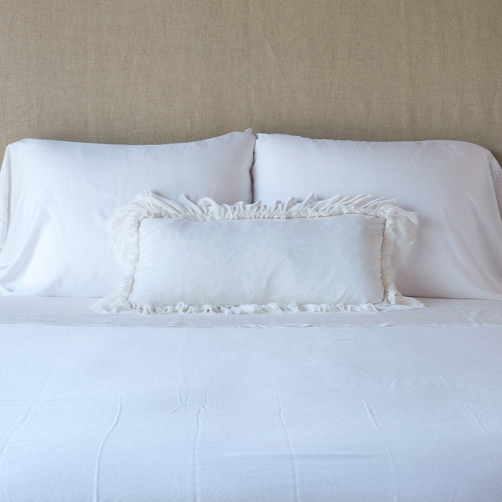 Loulah Throw Pillow | White | pillow on a white bed - cropped end of bed view.