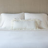 Loulah Throw Pillow | Winter White | pillow on a white bed - cropped end of bed view.