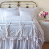 Loulah shams on a neatly made all-white bed with matching bolster and throw blanket - end of bed view.