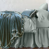 Loulah Blanket | Eucalyptus | throw blanket draped over a monochromatic bed, shown with matching throw pillow - side view.