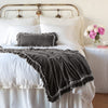 Loulah Blanket | Fog | Loulah throw blanket draped over the end of a white bed, shown with matching accent pillow - fog, end of bed view.