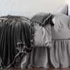 Loulah Blanket | Fog | throw blanket draped over a monochromatic bed, shown with matching throw pillow - side view.
