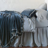 Loulah Blanket | Mineral | throw blanket draped over a monochromatic bed, shown with matching throw pillow - side view.