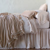 Loulah Blanket | Pearl | throw blanket draped over a monochromatic bed, shown with matching throw pillow - side view.