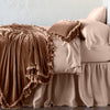Loulah Blanket | Rouge | throw blanket draped over a monochromatic bed, shown with matching throw pillow - side view.