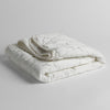 Luna Baby Blanket | White | quilted charmeuse blanket folded and shown against a white background from a slight overhead angle.