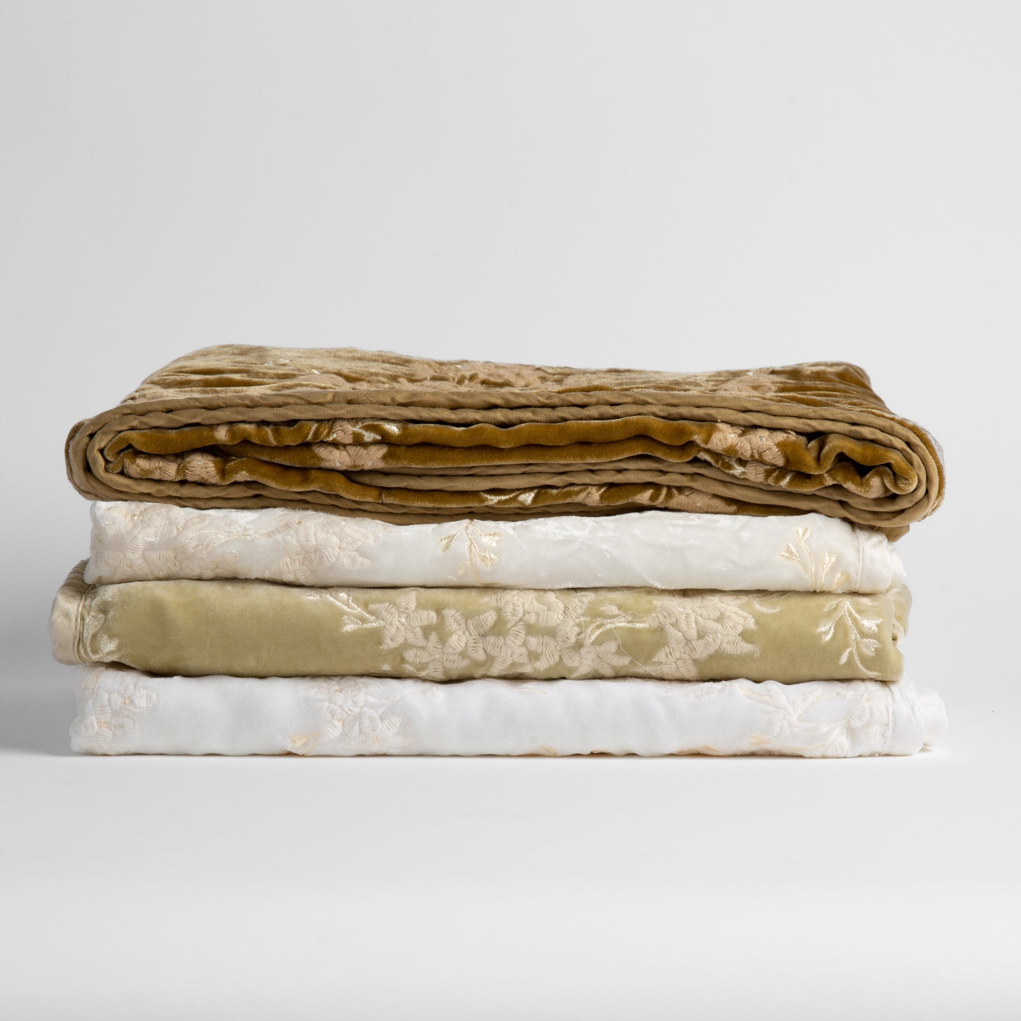 Lynette Baby Blanket | a stack of neutral and golden toned embroidered silk velvet baby blankets against a white background.