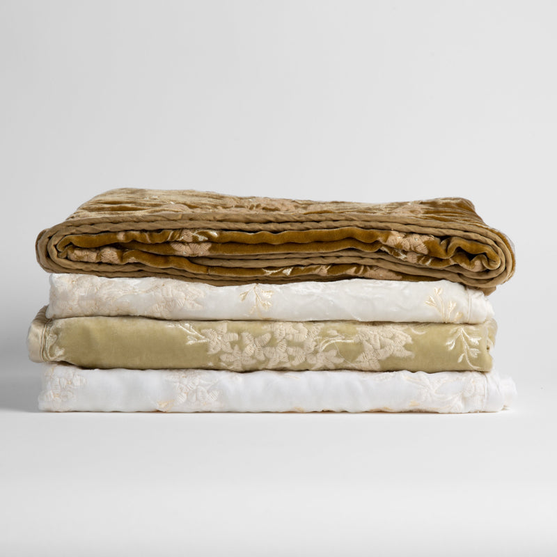 Lynette Baby Blanket | a stack of neutral and golden toned embroidered silk velvet baby blankets against a white background.