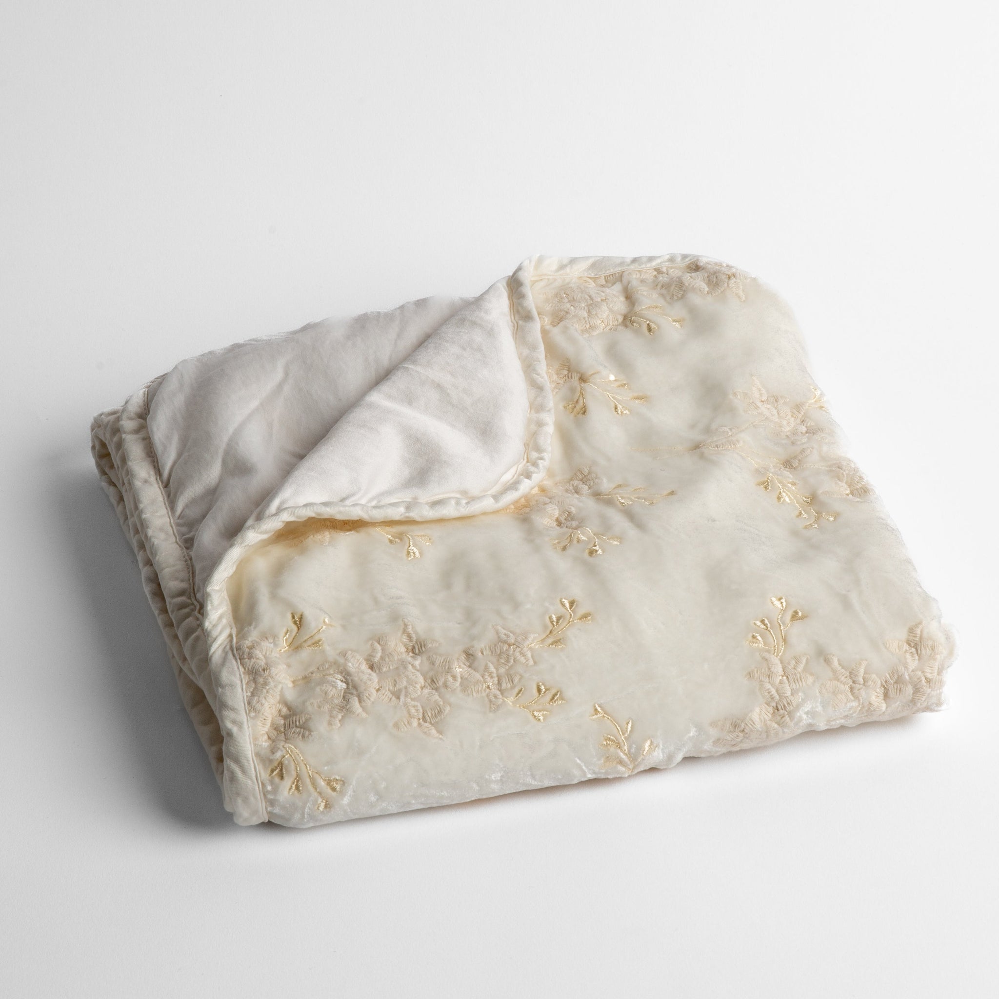 Lynette Baby Blanket | Winter White | embroidered silk velvet baby blanket folded with a corner folded back to show the trim and back of the blanket - shot overhead at a slight angle against a white background.