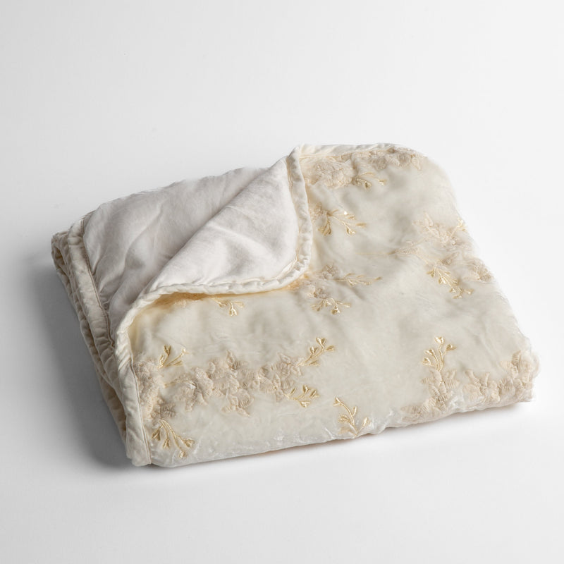 Lynette Baby Blanket | Winter White | embroidered silk velvet baby blanket folded with a corner folded back to show the trim and back of the blanket - shot overhead at a slight angle against a white background.