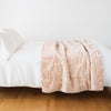 Lynette Blanket | Lynette throw blanket in pearl, draped over a simple white bed - side view.