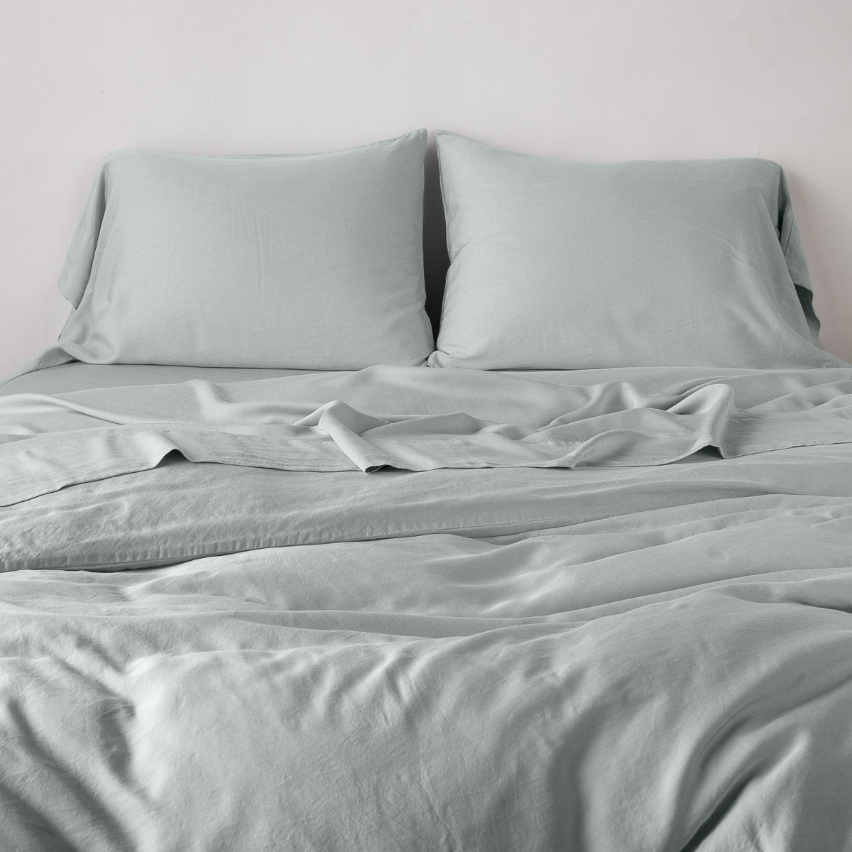 Madera Luxe Duvet Cover | Eucalyptus | duvet cover with matching sleeping pillows and sheeting against a white wall - end of bed view.