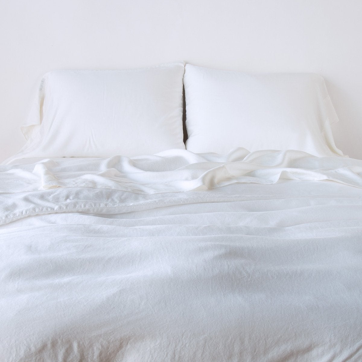 Madera Luxe Duvet Cover | White | duvet cover with matching sleeping pillows and sheeting against a white wall - end of bed view.