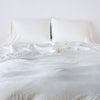 Madera Luxe Twin Duvet Cover | Madera Luxe duvet cover in winter white with monochromatic sheeting and sleeping pillows, agaisnt a plain white background - close-up end of bed view.