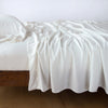 Madera Luxe Flat Sheet | Winter White | Rumpled flat sheet with matching fitted sheet and sleeping pillow - side view.