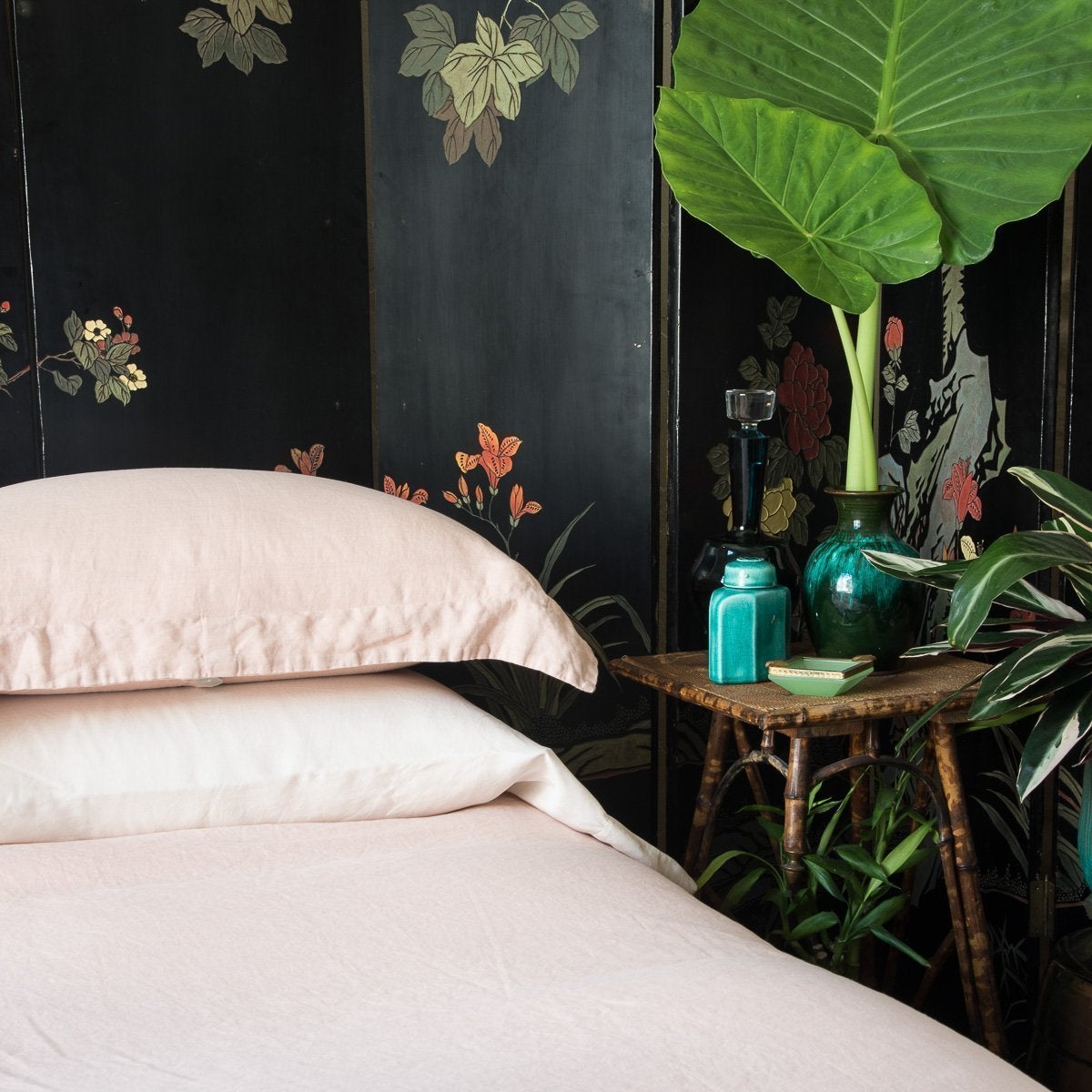 Madera Luxe Pillowcase (Single) | Pearl | Madera Luxe sleeping pillow laid flat under a linen sham, on a linen duvet cover, all in pearl, with a dark floral wall panel and tall greenery - cropped three-quarter angle.