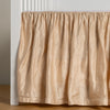 Paloma Crib Skirt | Pearl | charmeuse crib skirt shown on a white crib against a white wall and medium wood floor.