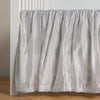 Paloma Crib Skirt | White | charmeuse crib skirt shown on a white crib against a white wall and medium wood floor.