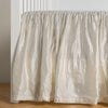 Paloma Crib Skirt | Winter White | charmeuse crib skirt shown on a white crib against a white wall and medium wood floor.