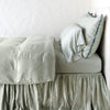 Eucalyptus | Paloma bed skirt, layered under a matching duvet cover and monochromatic sheeting - eucalyptus, side view.