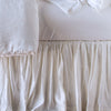 Close up of Paloma bed skirt, highlighting the shimmering fabric and the gathering detail - white, side view.