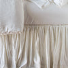 Close up of Paloma bed skirt, highlighting the shimmering fabric and the gathering detail - winter white, side view.