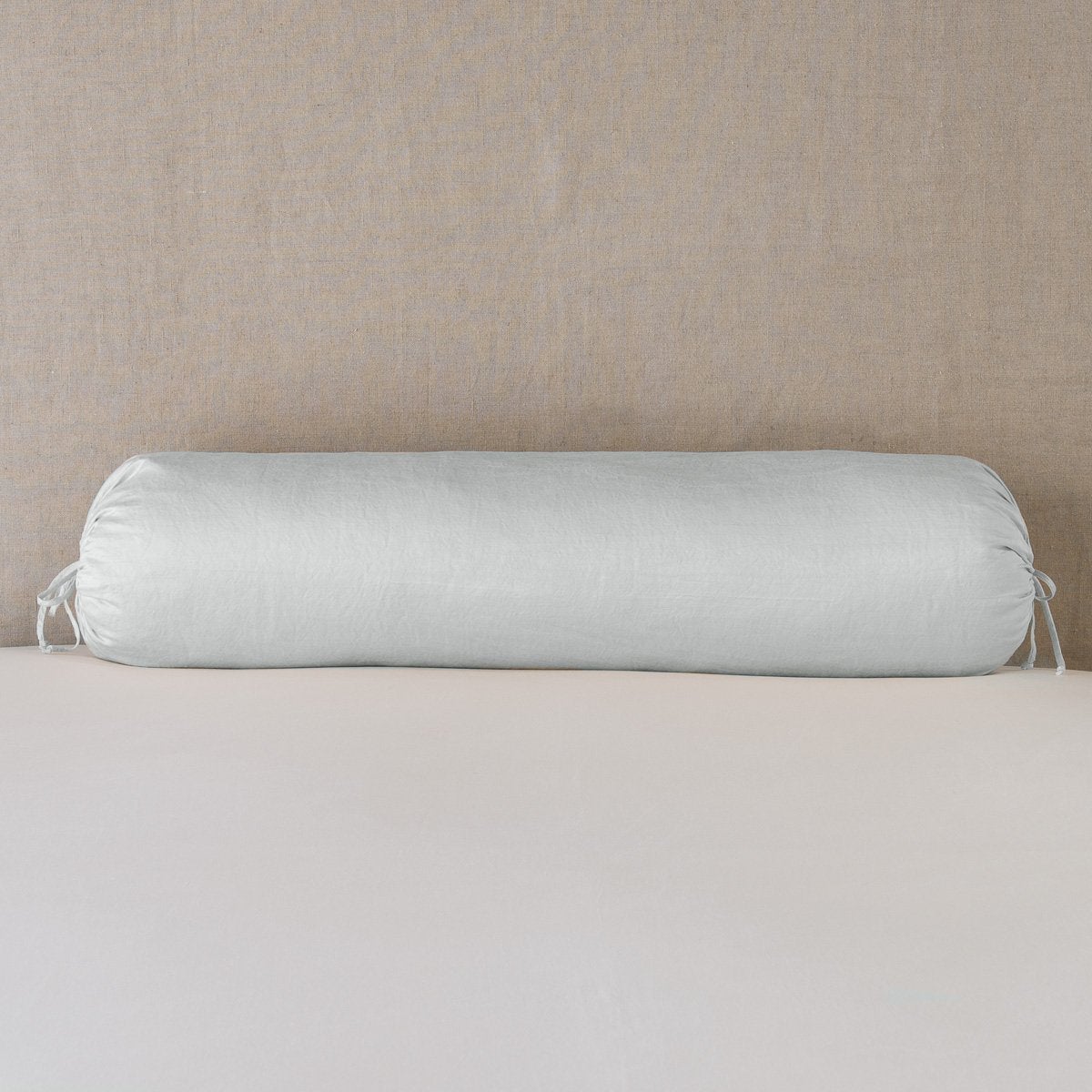 Paloma Throw Pillow | Cloud | bolster on white sheets with a neutral headboard.