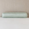 Paloma Throw Pillow | Eucalyptus | bolster on white sheets with a neutral headboard.
