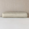 Paloma Throw Pillow | Fog | bolster on white sheets with a neutral headboard.