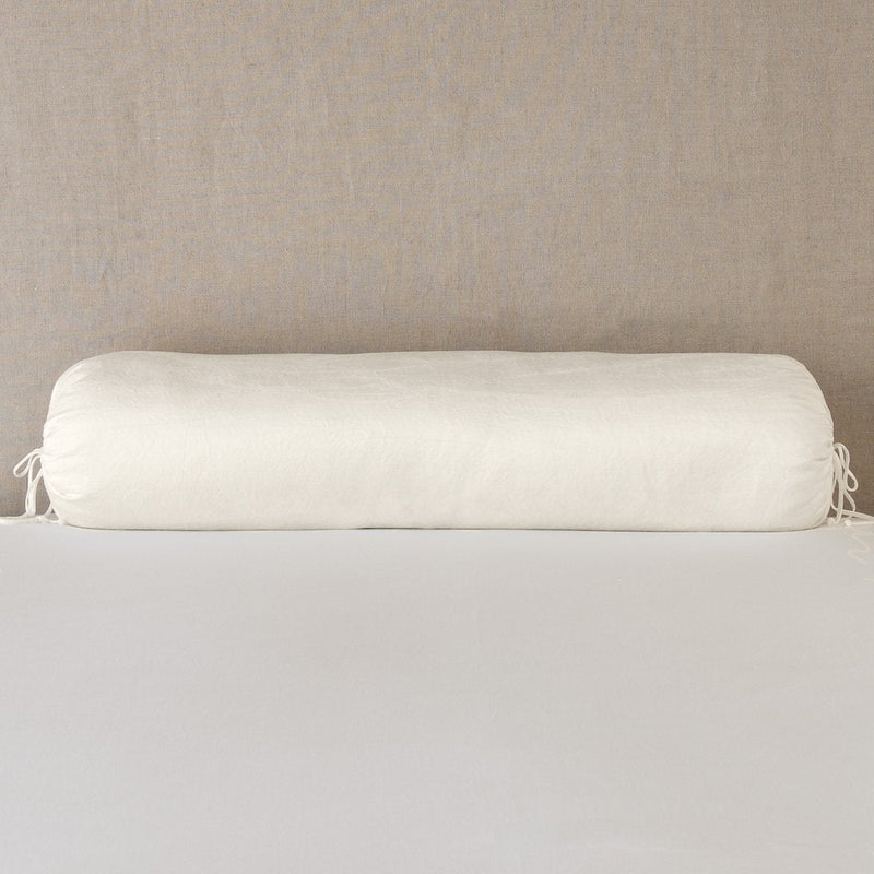 Paloma Throw Pillow | Parchment | bolster on white sheets with a neutral headboard.